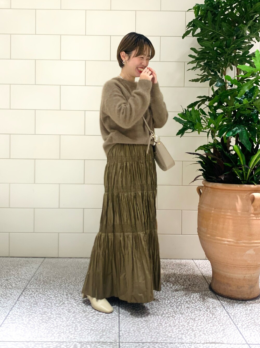 イエロー系のカーディガン/ボレロ、ブラウン系のスカート、ベージュ系のショルダーバッグを着用したレディースの冬コーディネートの1枚目の写真