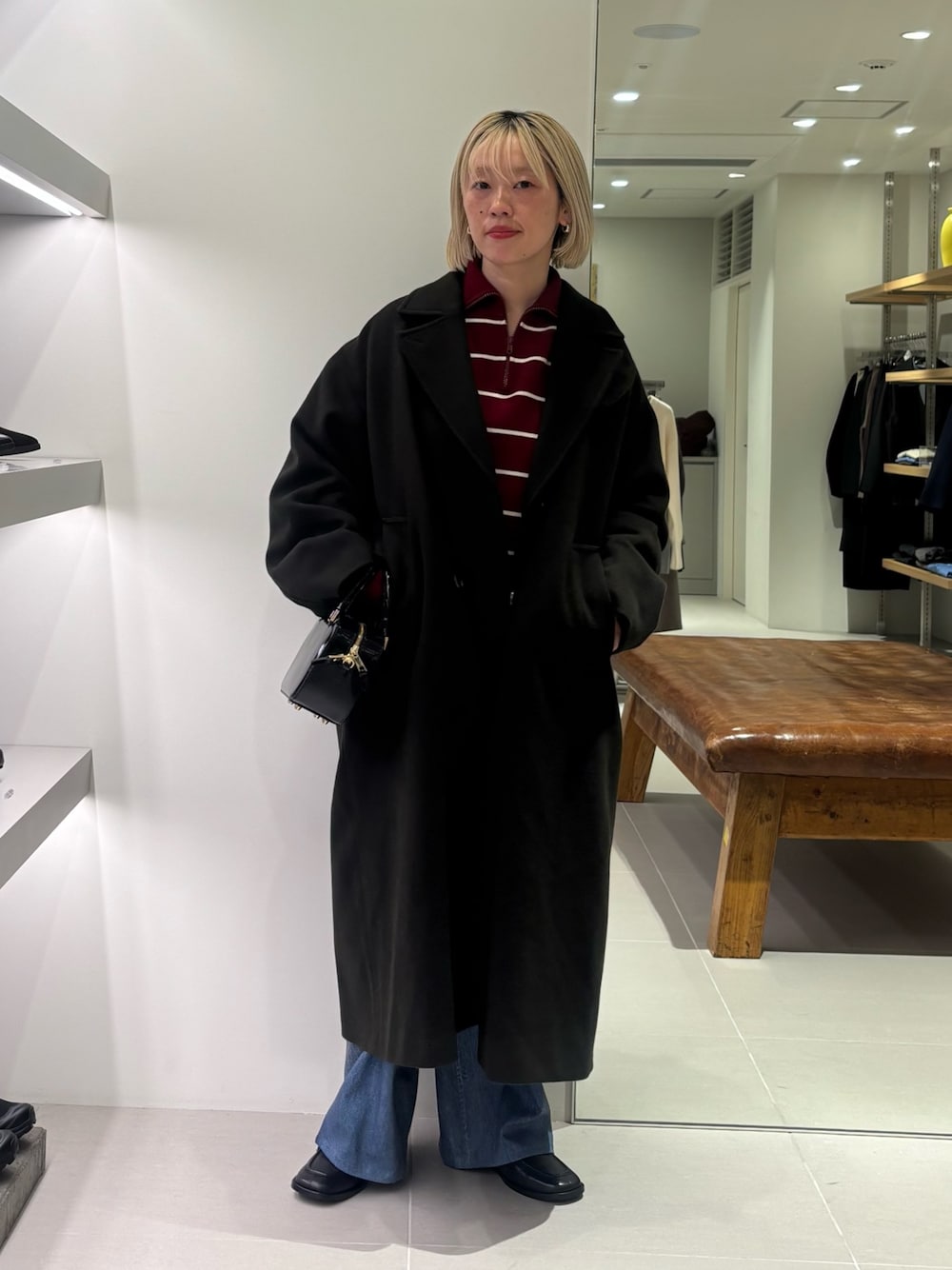 グリーン系のチェスターコート、ブルー系のその他パンツ、ブラック系のショルダーバッグを着用したレディースの秋コーディネートの1枚目の写真