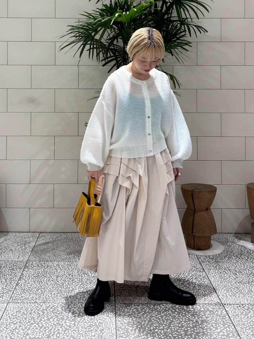 ホワイト系のスカート、ホワイト系のカーディガン/ボレロ、イエロー系のハンドバッグを着用したレディースの冬コーディネートの1枚目の写真