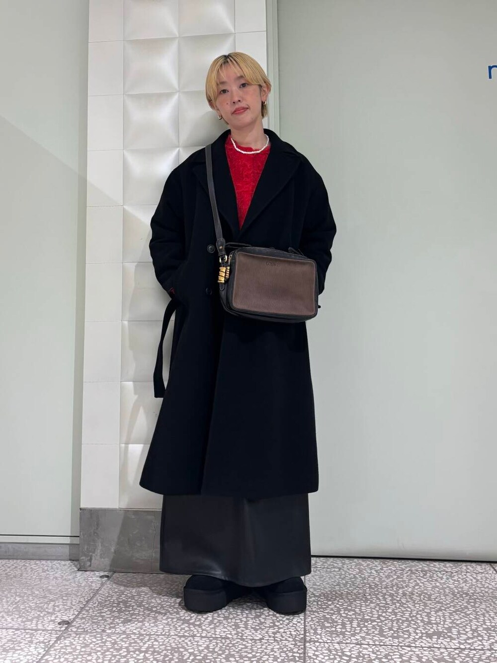 ブラック系のチェスターコート、ブラック系のスカート、ブラック系のブーツを着用したレディースの秋コーディネートの1枚目の写真