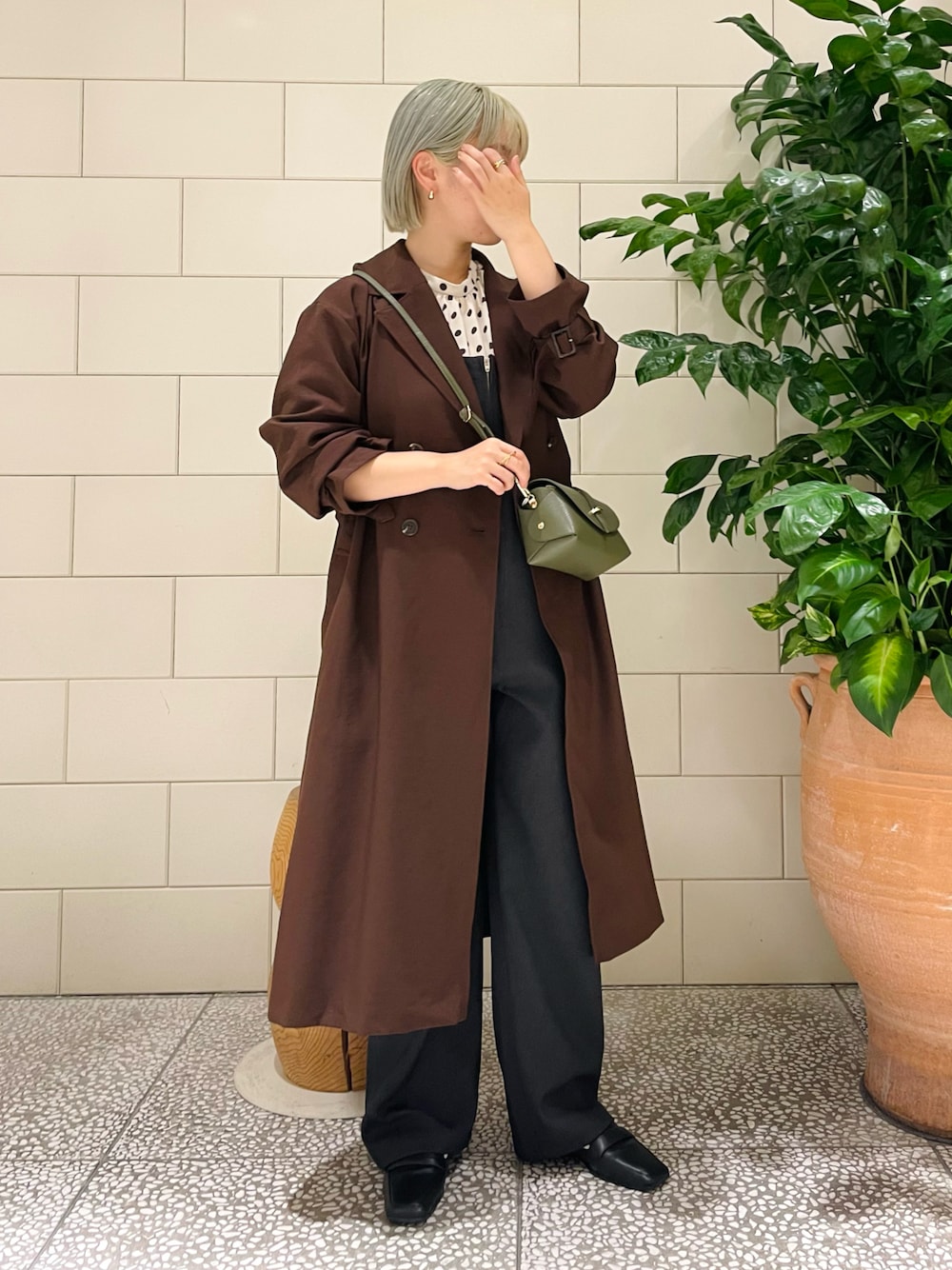 ブラウン系のトレンチコート、ホワイト系のシャツ/ブラウス、グリーン系のショルダーバッグを着用したレディースの秋コーディネートの1枚目の写真
