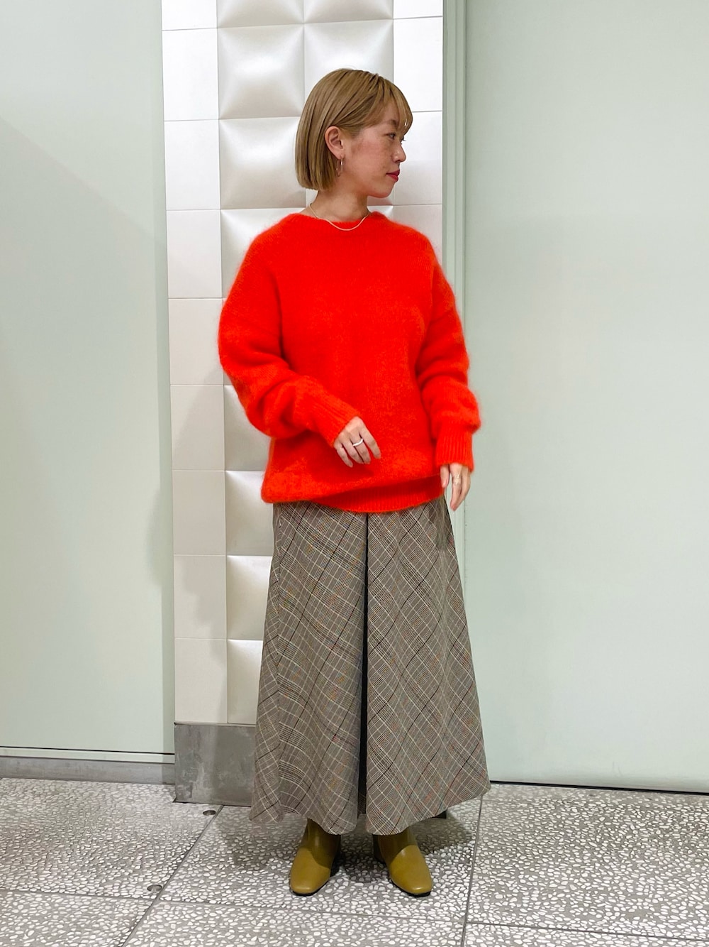 オレンジ系のニット/セーター、ベージュ系のスカート、ベージュ系のブーツを着用したレディースの秋コーディネートの1枚目の写真