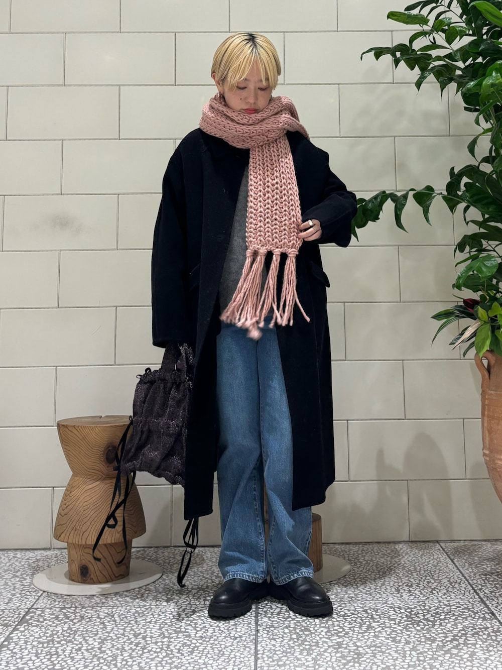 ブラック系のステンカラーコート、グレー系のニット/セーター、ブルー系のデニムパンツを着用したレディースの秋コーディネートの1枚目の写真