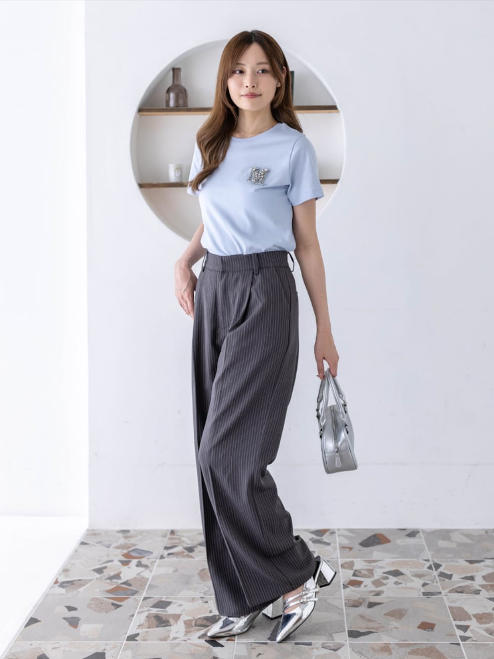 シルバー系のパンプス、グレー系のスラックス、ブルー系のTシャツ/カットソーを着用したレディースの春コーディネートの1枚目の写真