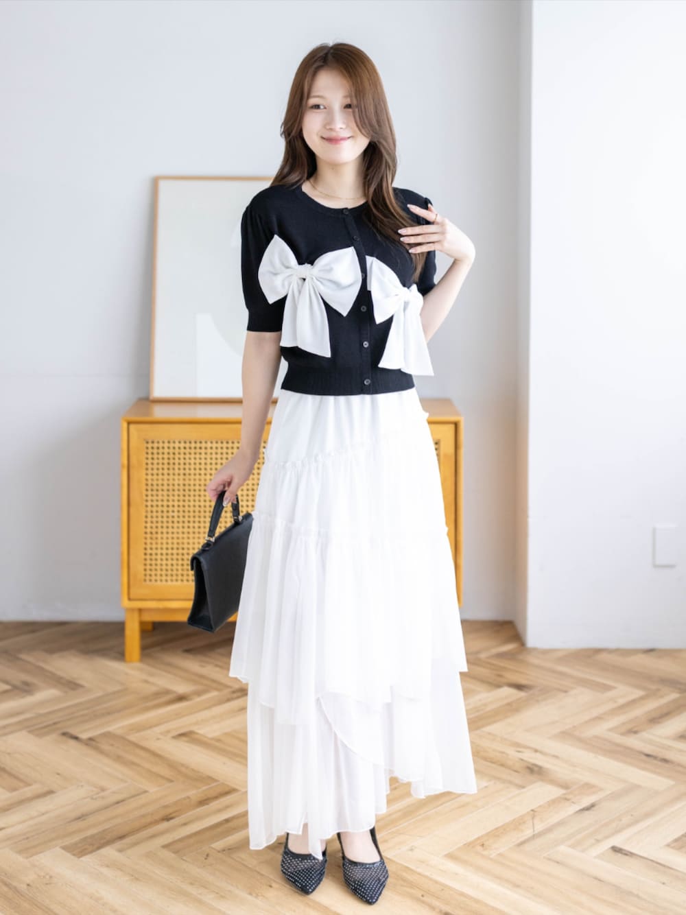ブラック系のハンドバッグ、ブラック系のパンプス、ホワイト系のスカートを着用したレディースの夏コーディネートの1枚目の写真