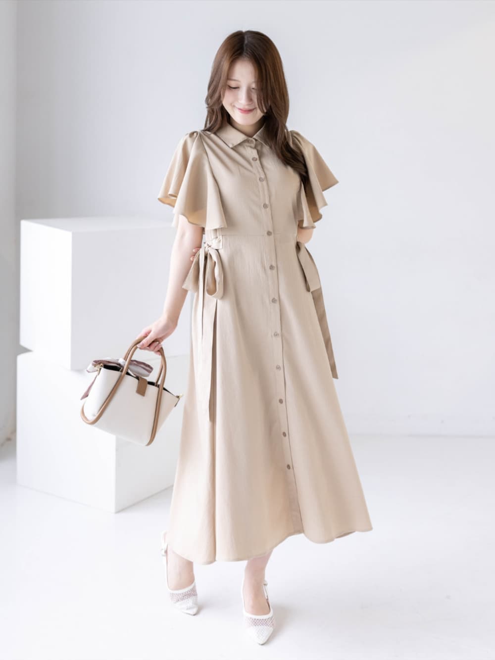 ホワイト系のパンプス、ベージュ系のワンピース、ベージュ系のハンドバッグを着用したレディースの夏コーディネートの1枚目の写真