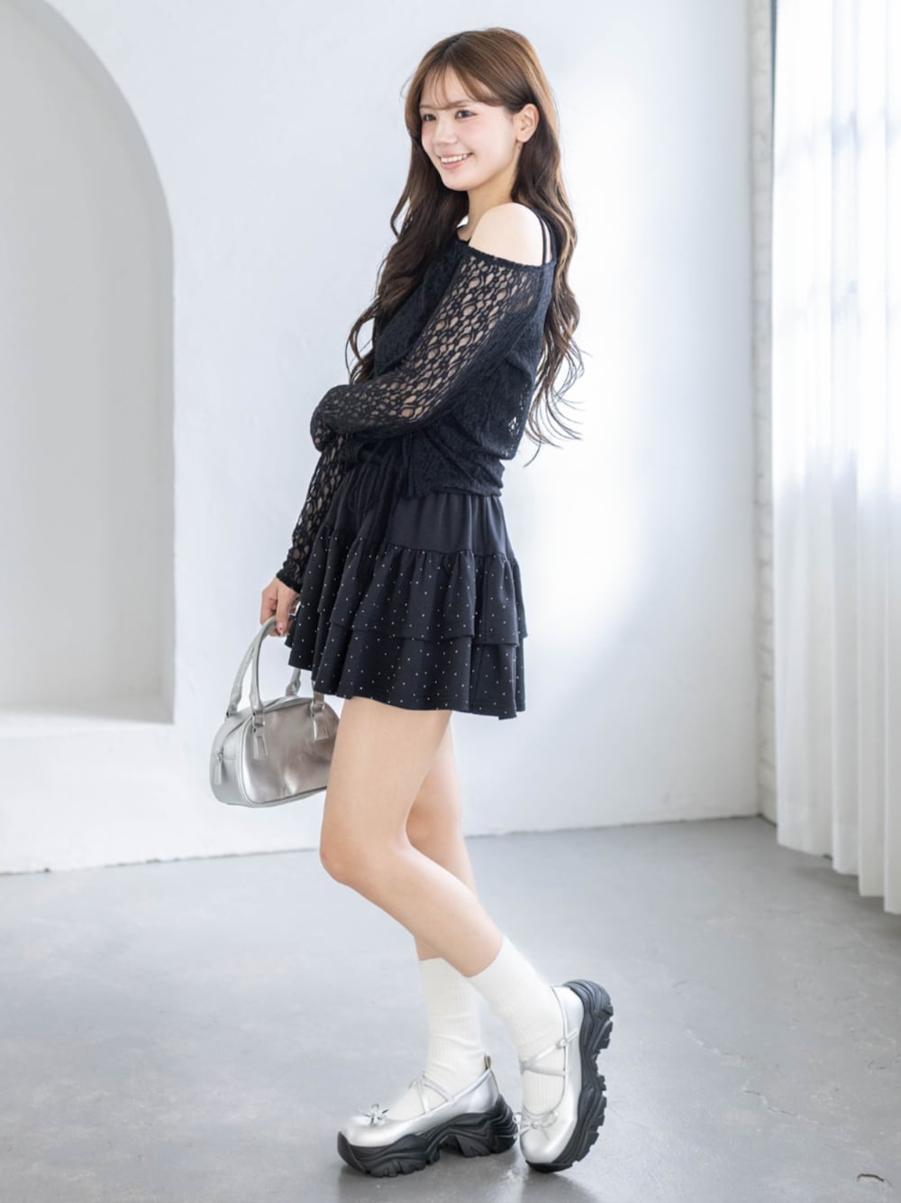 シルバー系のハンドバッグ、ブラック系のアンサンブル、ブラック系のスカートを着用したレディースの春コーディネートの1枚目の写真