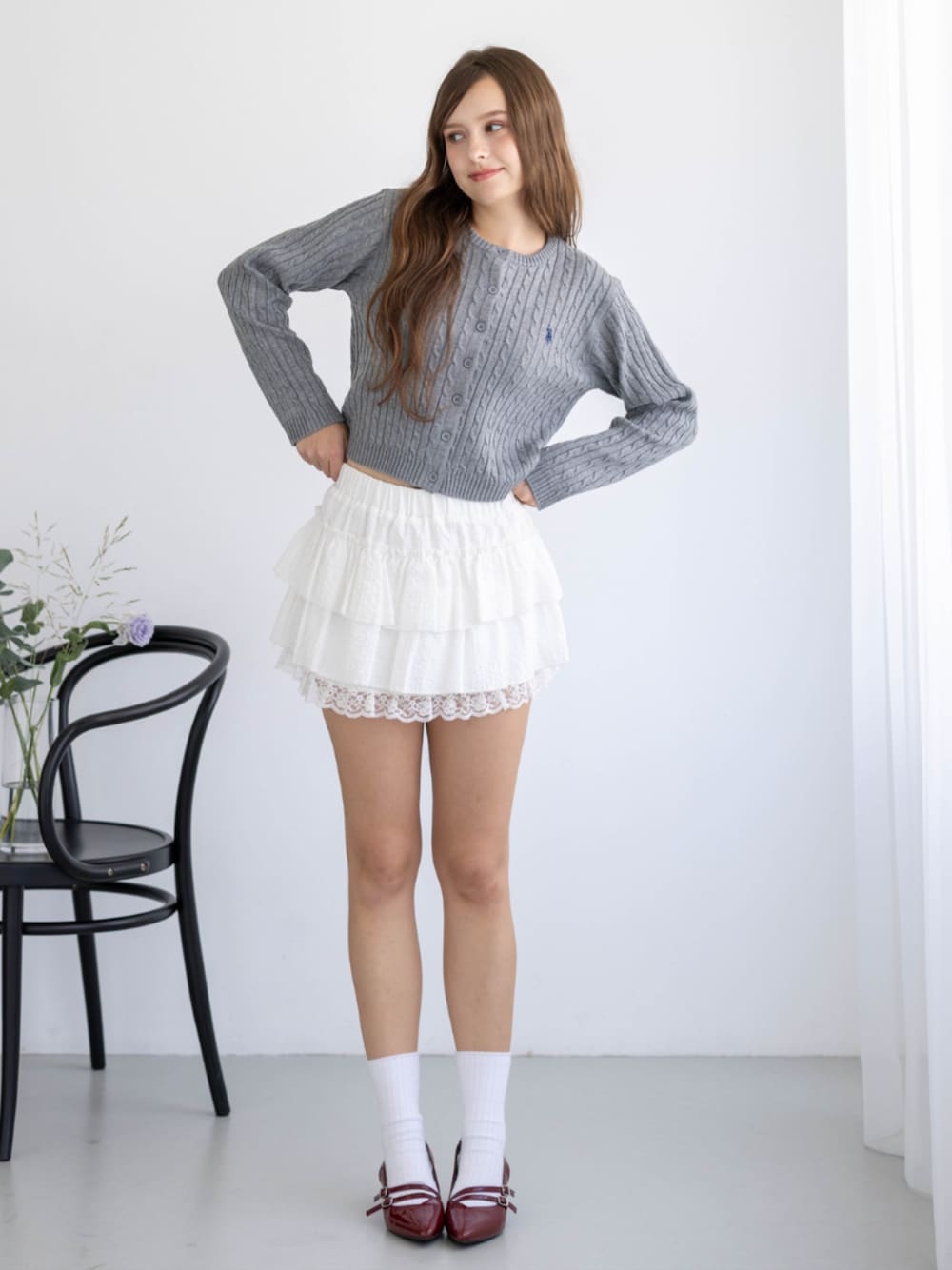 レッド系のパンプス、グレー系のカーディガン/ボレロ、ホワイト系のスカートを着用したレディースの秋コーディネートの1枚目の写真