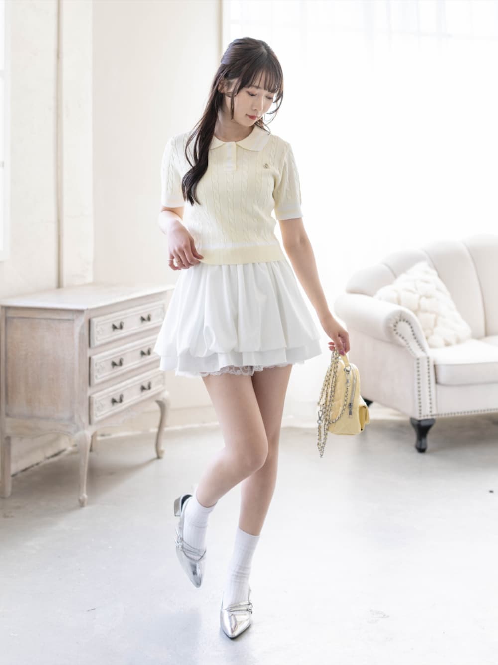 シルバー系のパンプス、ホワイト系のスカート、イエロー系のニット/セーターを着用したレディースの夏コーディネートの1枚目の写真
