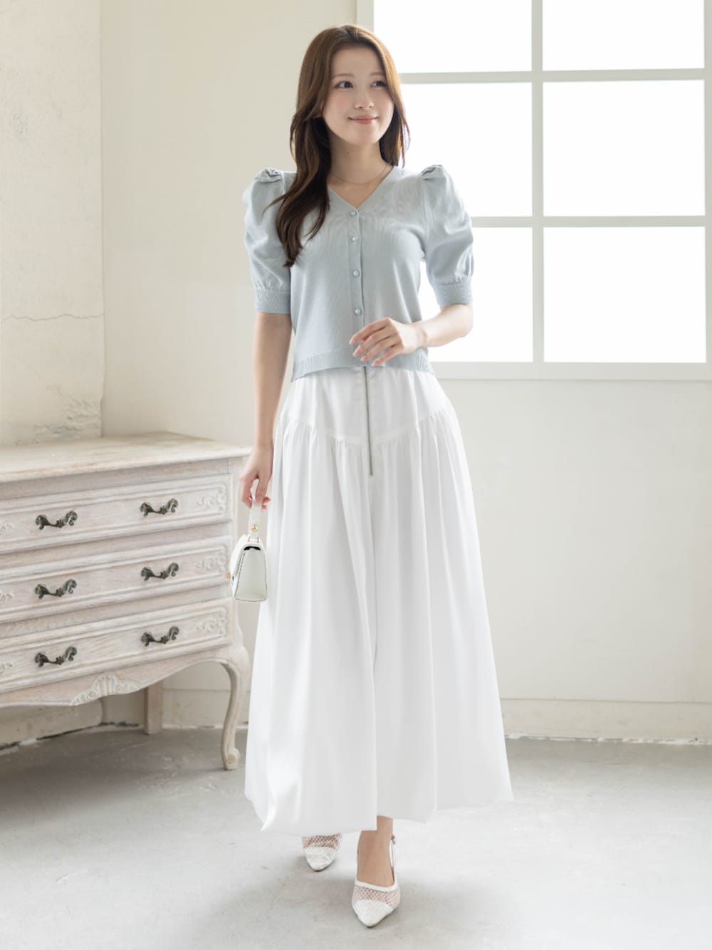 ホワイト系のスカート、ホワイト系のパンプス、グレー系のカーディガン/ボレロを着用したレディースの春コーディネートの1枚目の写真