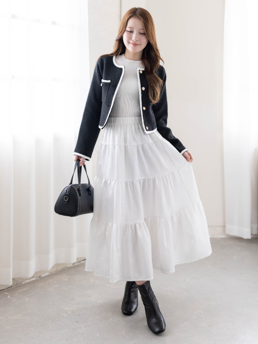 ブラック系のノーカラージャケット、ホワイト系のスカートを着用したレディースの冬コーディネートの1枚目の写真