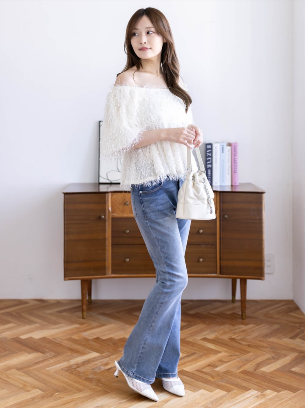 ブルー系のデニムパンツ、ホワイト系のハンドバッグ、ホワイト系のパンプスを着用したレディースの春コーディネートの1枚目の写真