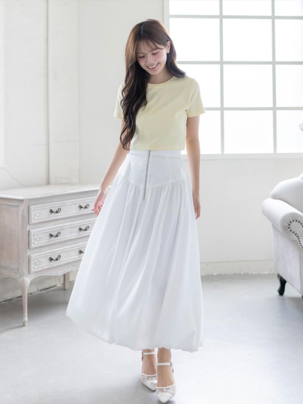 ホワイト系のスカート、ホワイト系のパンプス、イエロー系のTシャツ/カットソーを着用したレディースの夏コーディネートの1枚目の写真