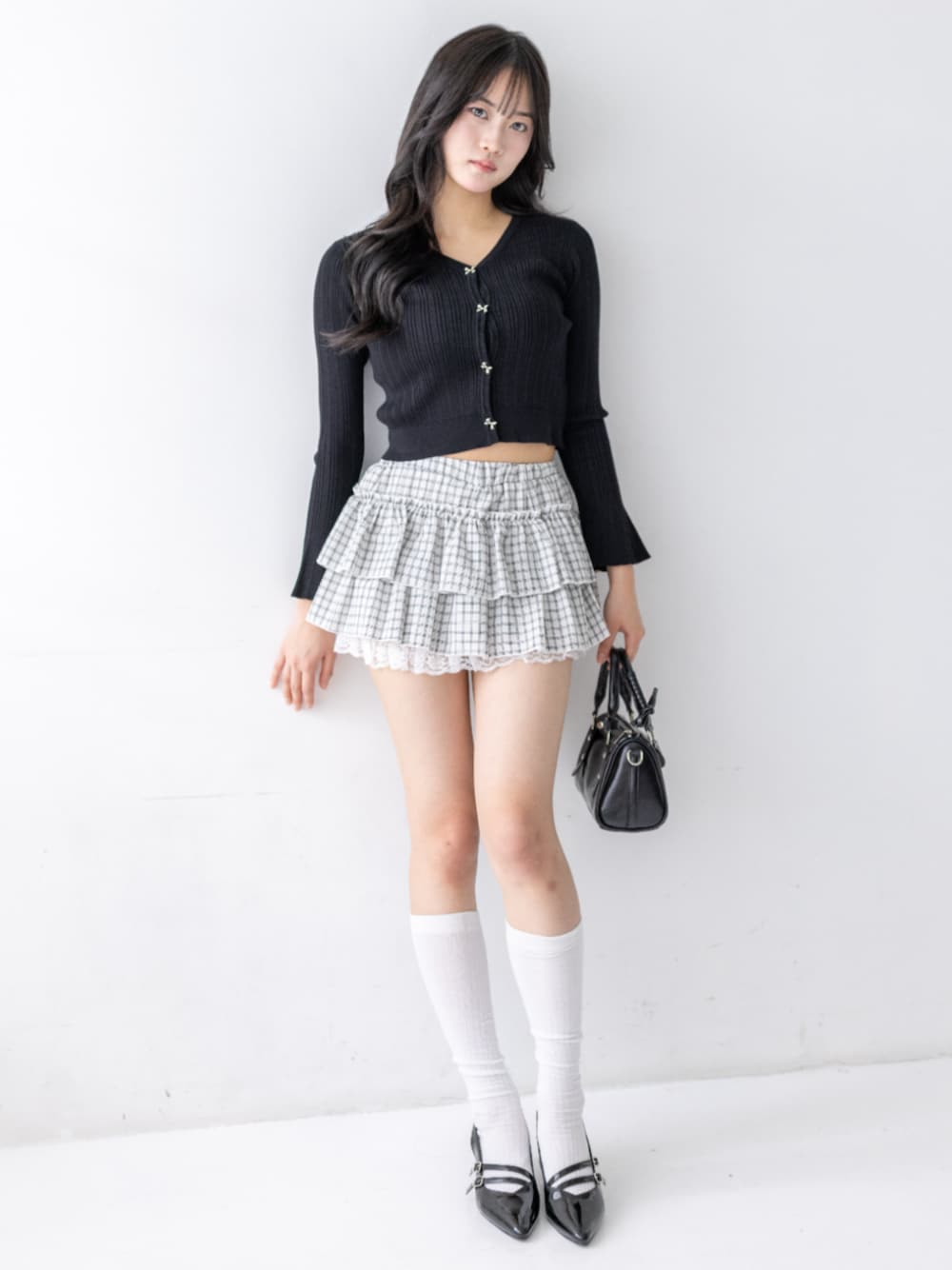 ブラック系のパンプス、ブラック系のハンドバッグ、ホワイト系のスカートを着用したレディースの夏コーディネートの1枚目の写真