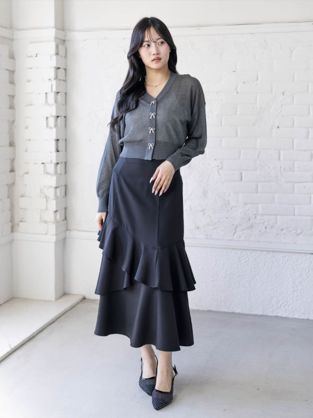 ブラック系のパンプス、ブラック系のスカート、グレー系のカーディガン/ボレロを着用したレディースの春コーディネートの1枚目の写真