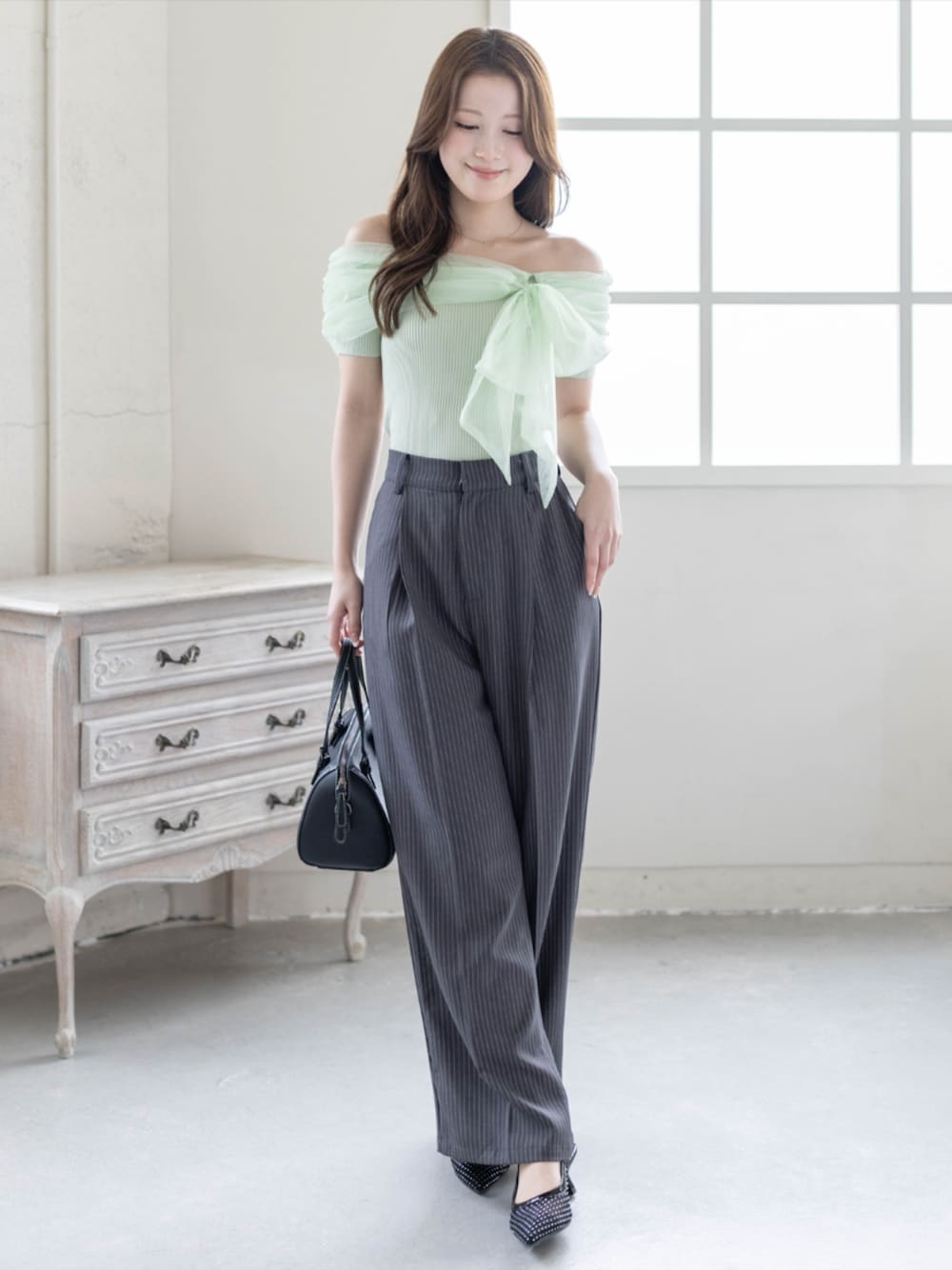 ブラック系のボストンバッグ、ブラック系のパンプス、グレー系のスラックスを着用したレディースの春コーディネートの1枚目の写真