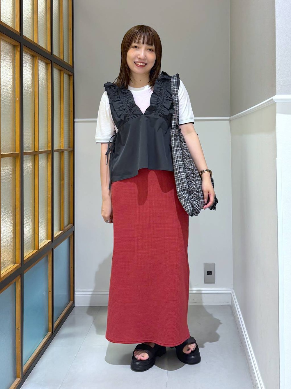 レッド系のスカート、ブラック系のトートバッグ、ブラウン系のサンダルを着用したレディースの夏コーディネートの1枚目の写真
