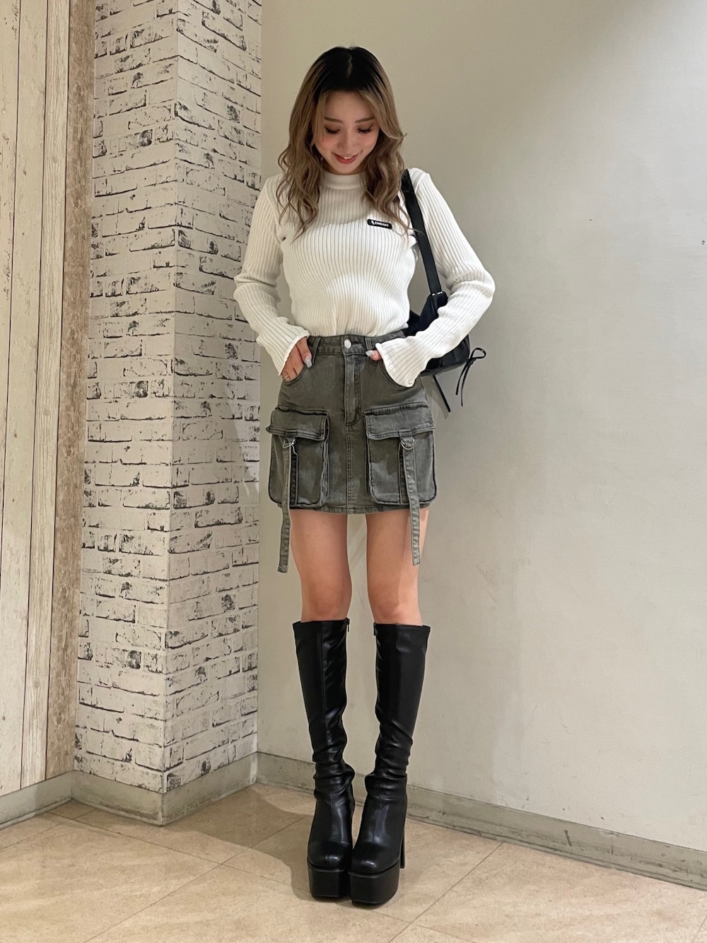 ホワイト系のニット/セーター、ブラック系のデニムスカート、ブラック系のブーツを着用したレディースの秋コーディネートの1枚目の写真