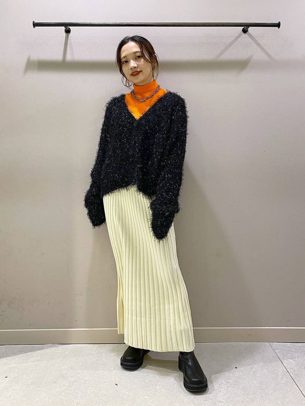 オレンジ系のニット/セーター、ブラック系のブーツ、ホワイト系のワンピースを着用したレディースの秋コーディネートの1枚目の写真