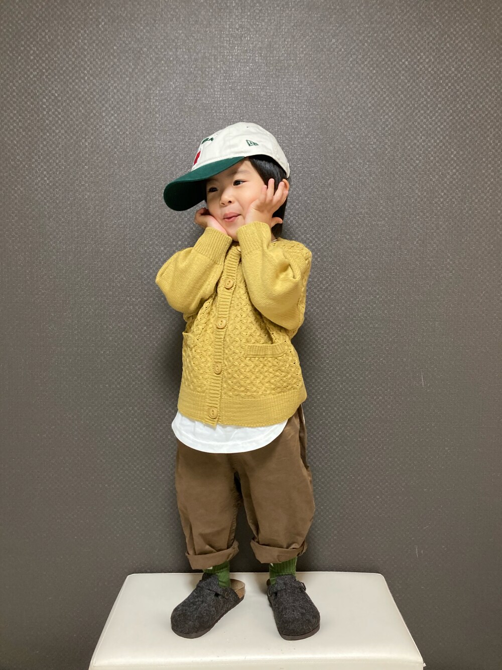 イエロー系のカーディガン/ボレロ、ブラウン系のチノパンツ、グレー系のサンダルを着用したキッズの冬コーディネートの1枚目の写真