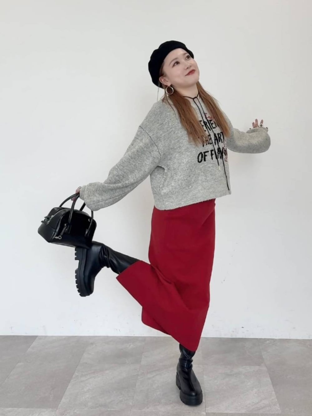 レッド系のスカート、ブラック系のブーツ、ブラック系のボストンバッグを着用したレディースの秋コーディネートの1枚目の写真