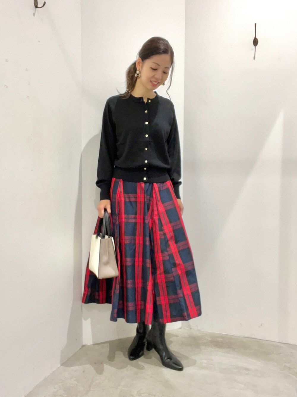 レッド系のスカート、ブラック系のカーディガン/ボレロ、ブラウン系のシューズを着用したレディースの秋コーディネートの1枚目の写真