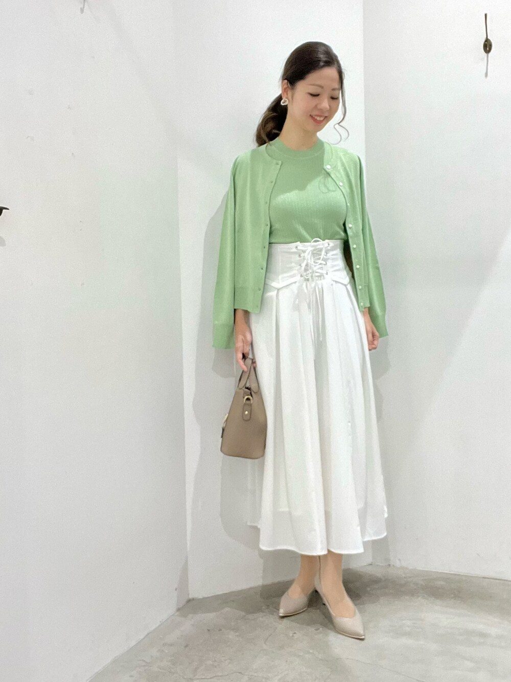 グリーン系のカーディガン/ボレロ、グリーン系のニット/セーター、ホワイト系のスカートを着用したレディースの春コーディネートの1枚目の写真
