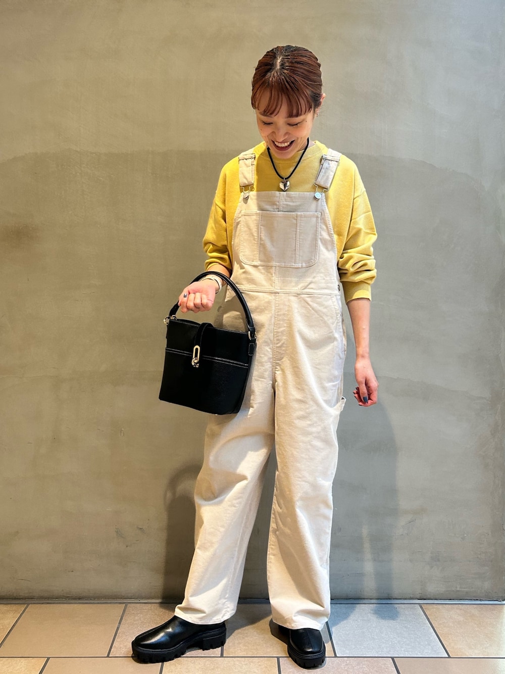 ホワイト系のサロペット/オーバーオール、イエロー系のニット/セーター、ブラック系のハンドバッグを着用したレディースの秋コーディネートの1枚目の写真