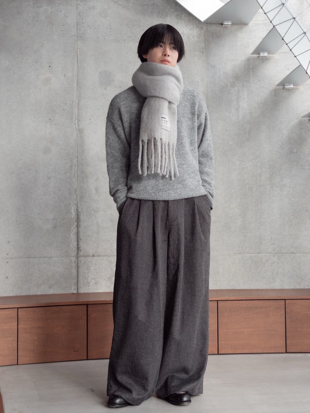 ブラック系のスラックス、ブラウン系のニット/セーター、グレー系のマフラーを着用したメンズの秋コーディネートの1枚目の写真