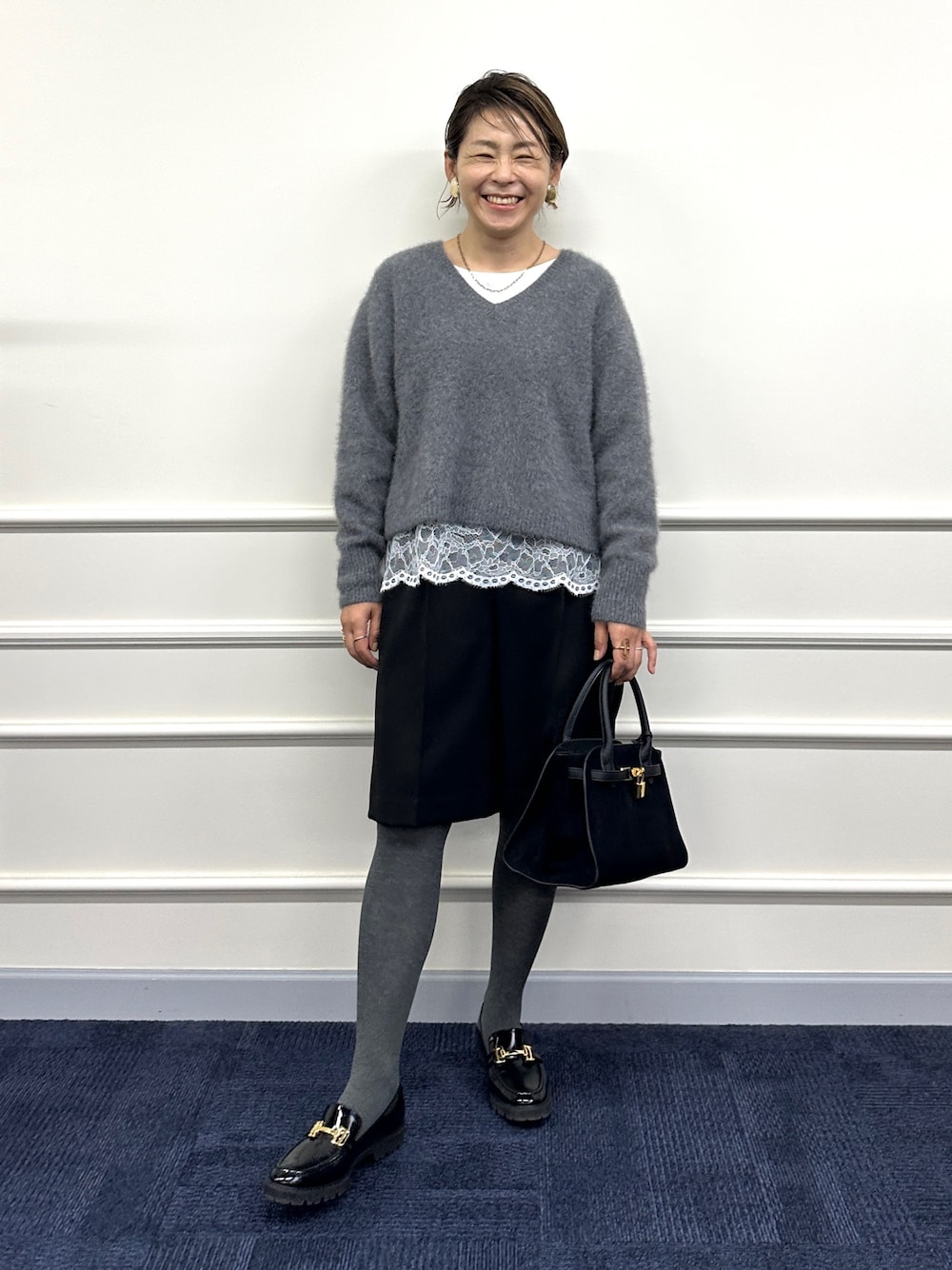 グレー系のニット/セーター、ホワイト系のシャツ/ブラウス、ブラック系のその他パンツを着用したレディースの秋コーディネートの1枚目の写真