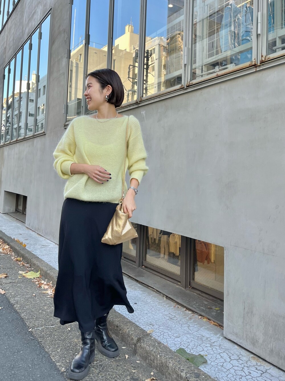 ゴールド系のクラッチバッグ、イエロー系のニット/セーター、ブラック系のスカートを着用したレディースの冬コーディネートの1枚目の写真