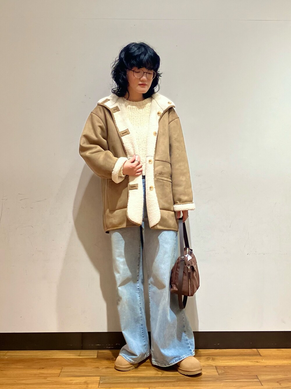 ブルー系のデニムパンツ、ブラウン系のショルダーバッグ、ホワイト系のムートンコートを着用したレディースの冬コーディネートの1枚目の写真
