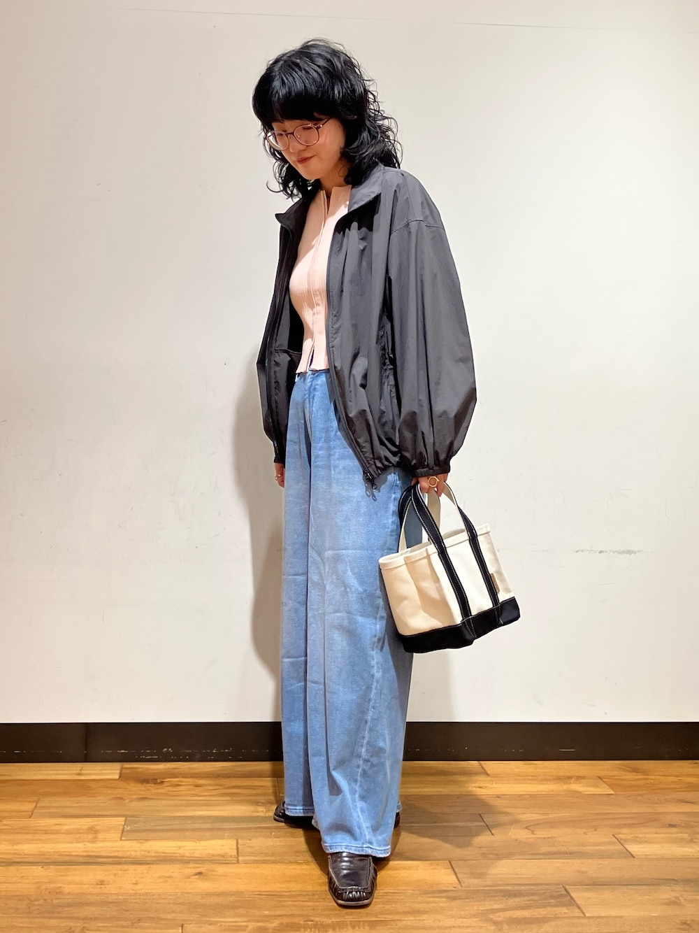 ブラック系のトートバッグ、ブルー系のデニムパンツ、グレー系のブルゾンを着用したレディースの春コーディネートの1枚目の写真