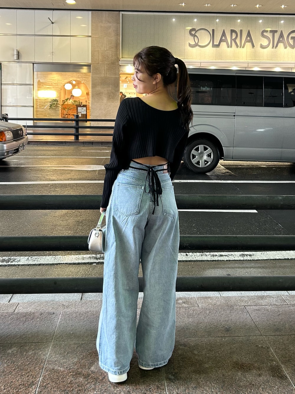 ブルー系のデニムパンツ、ブラック系のニット/セーター、シルバー系のショルダーバッグを着用したレディースの冬コーディネートの1枚目の写真