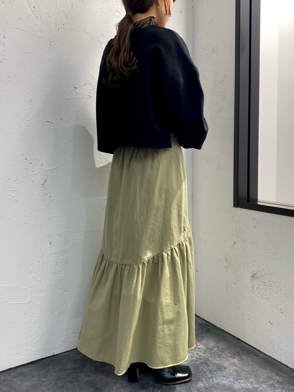 グリーン系のスカート、ブラック系のニット/セーター、ブラック系のTシャツ/カットソーを着用したレディースの冬コーディネートの2枚目の写真