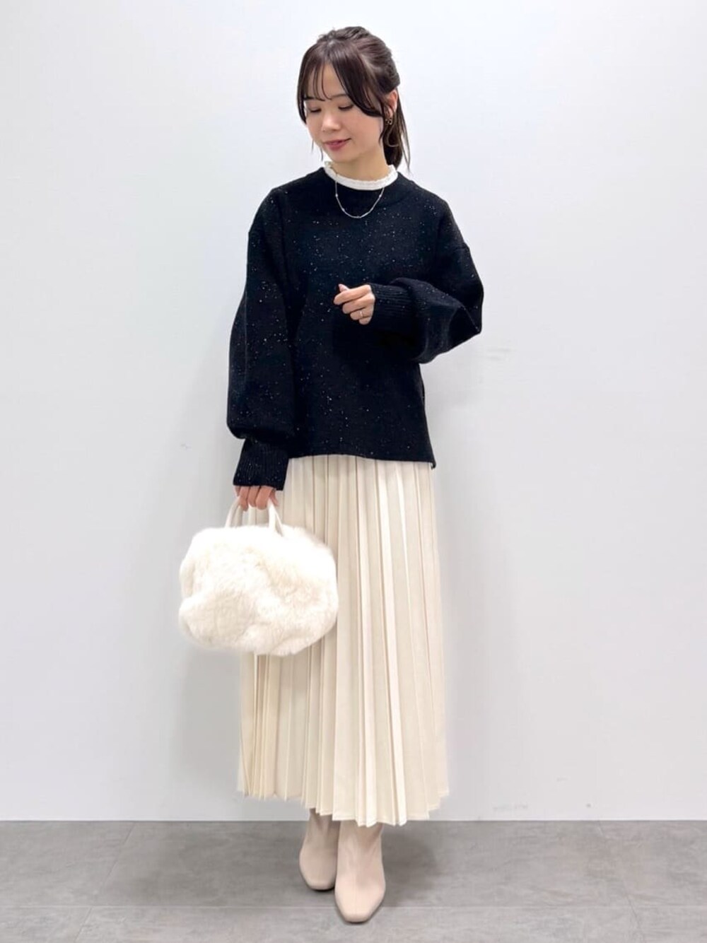 ブラック系のニット/セーター、ホワイト系のTシャツ/カットソー、ホワイト系のスカートを着用したレディースの冬コーディネートの1枚目の写真