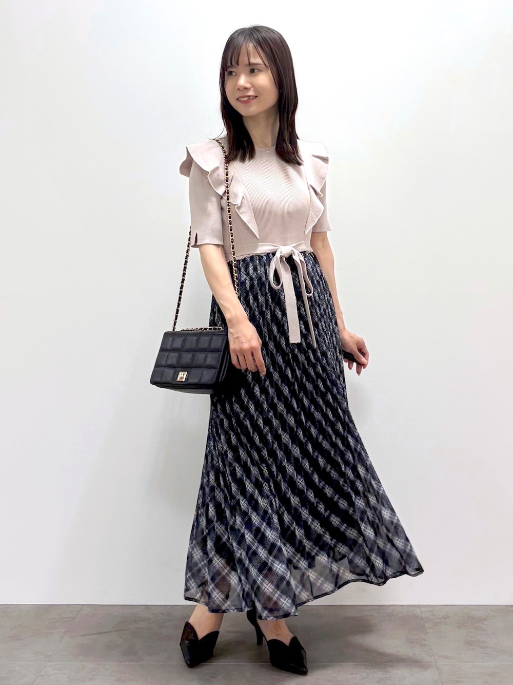 ブラック系のショルダーバッグ、ブラック系のパンプス、ゴールド系のネックレスを着用したレディースの春コーディネートの1枚目の写真