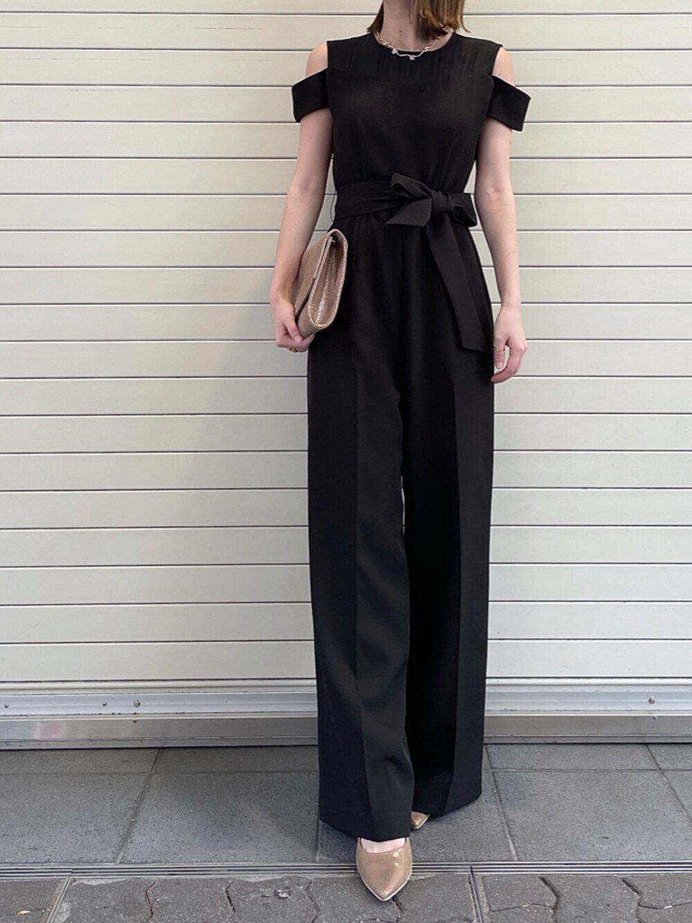 ブラック系のパンツドレス、ゴールド系のネックレスを着用したレディースの春コーディネートの1枚目の写真