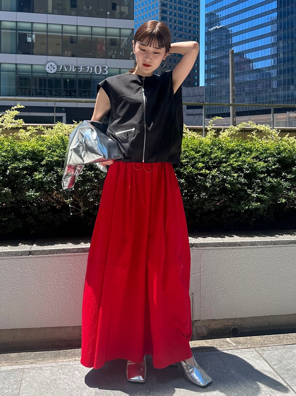 レッド系のスカート、シルバー系のパンプス、シルバー系のトートバッグを着用したレディースの夏コーディネートの1枚目の写真