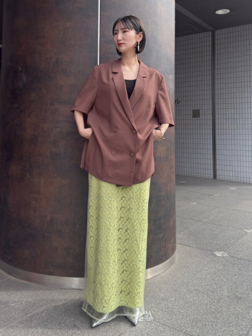 シルバー系のパンプス、ブラウン系のテーラードジャケット、グリーン系のスカートを着用したレディースの春コーディネートの1枚目の写真