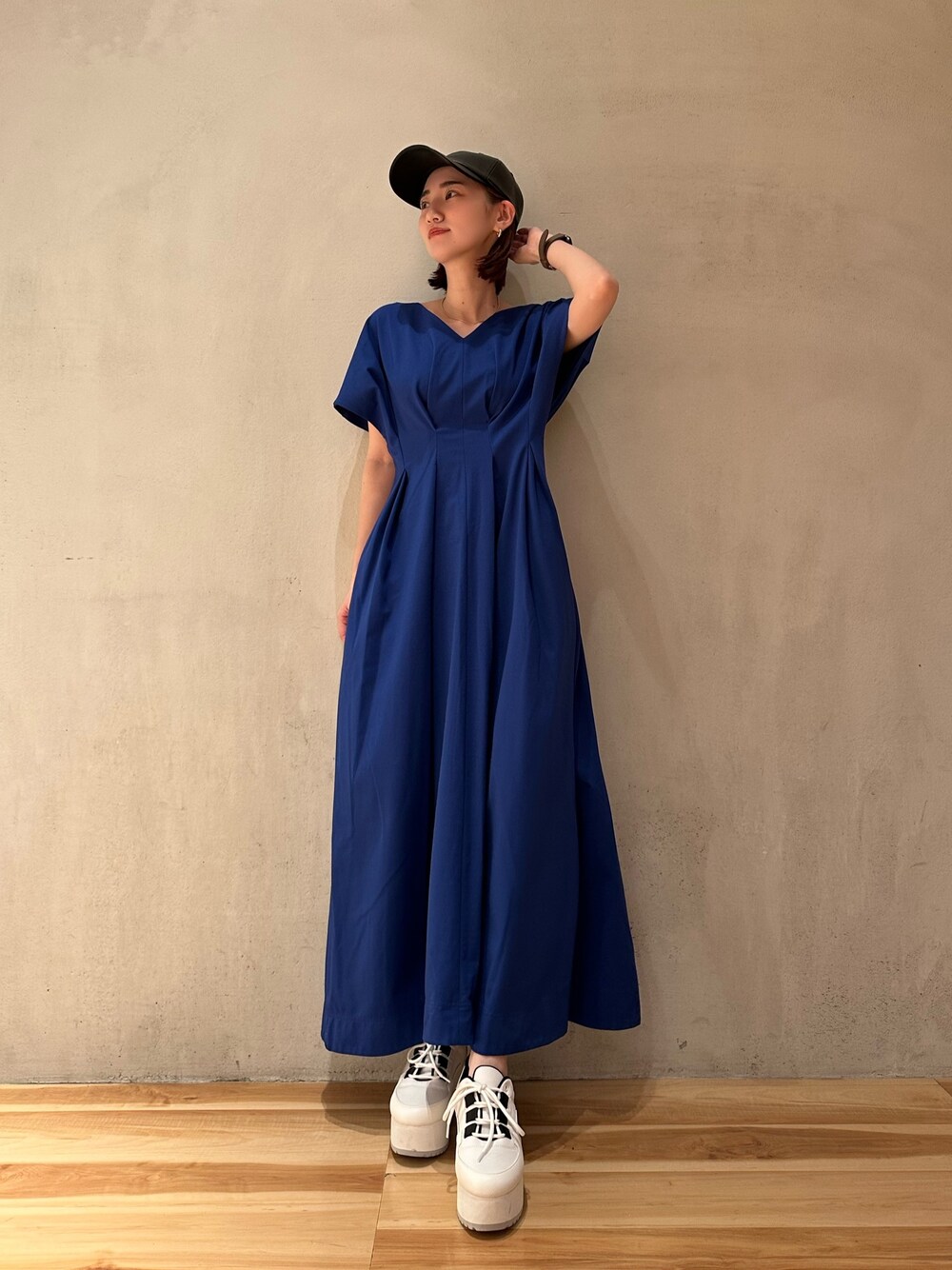 ブルー系のワンピース、ホワイト系のスニーカー、ブラック系のキャップを着用したレディースの春コーディネートの1枚目の写真