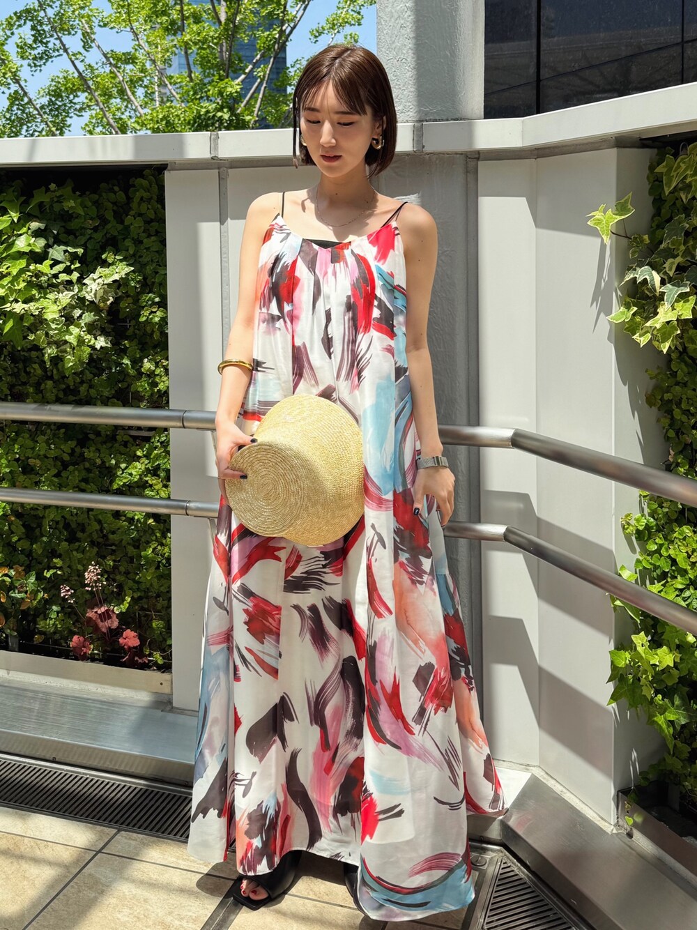 レッド系のワンピース、ブラック系のサンダル、ベージュ系のハットを着用したレディースの春コーディネートの1枚目の写真
