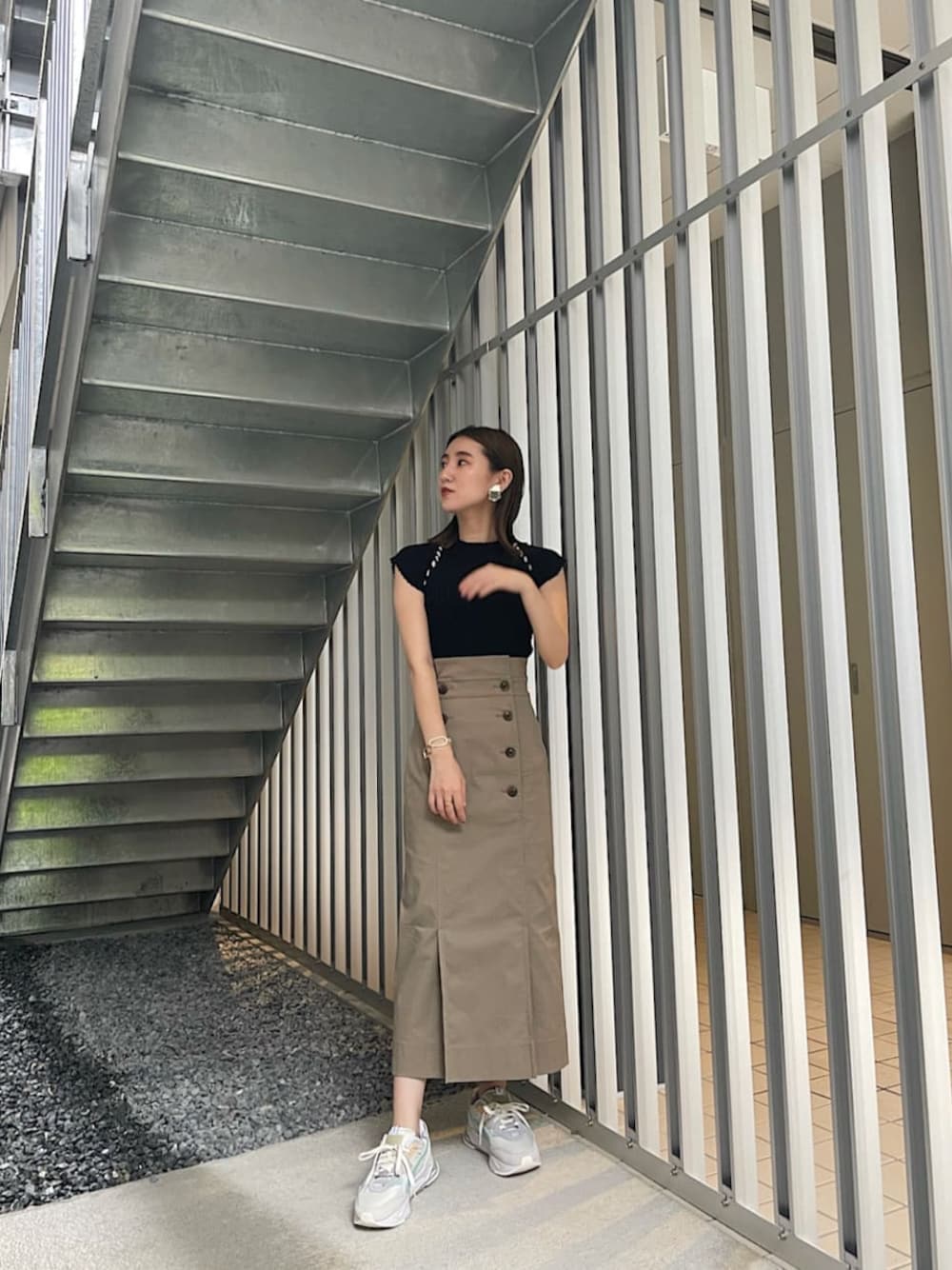 グレー系のスカート、ホワイト系のスニーカー、ブラック系のニット/セーターを着用したレディースの夏コーディネートの1枚目の写真