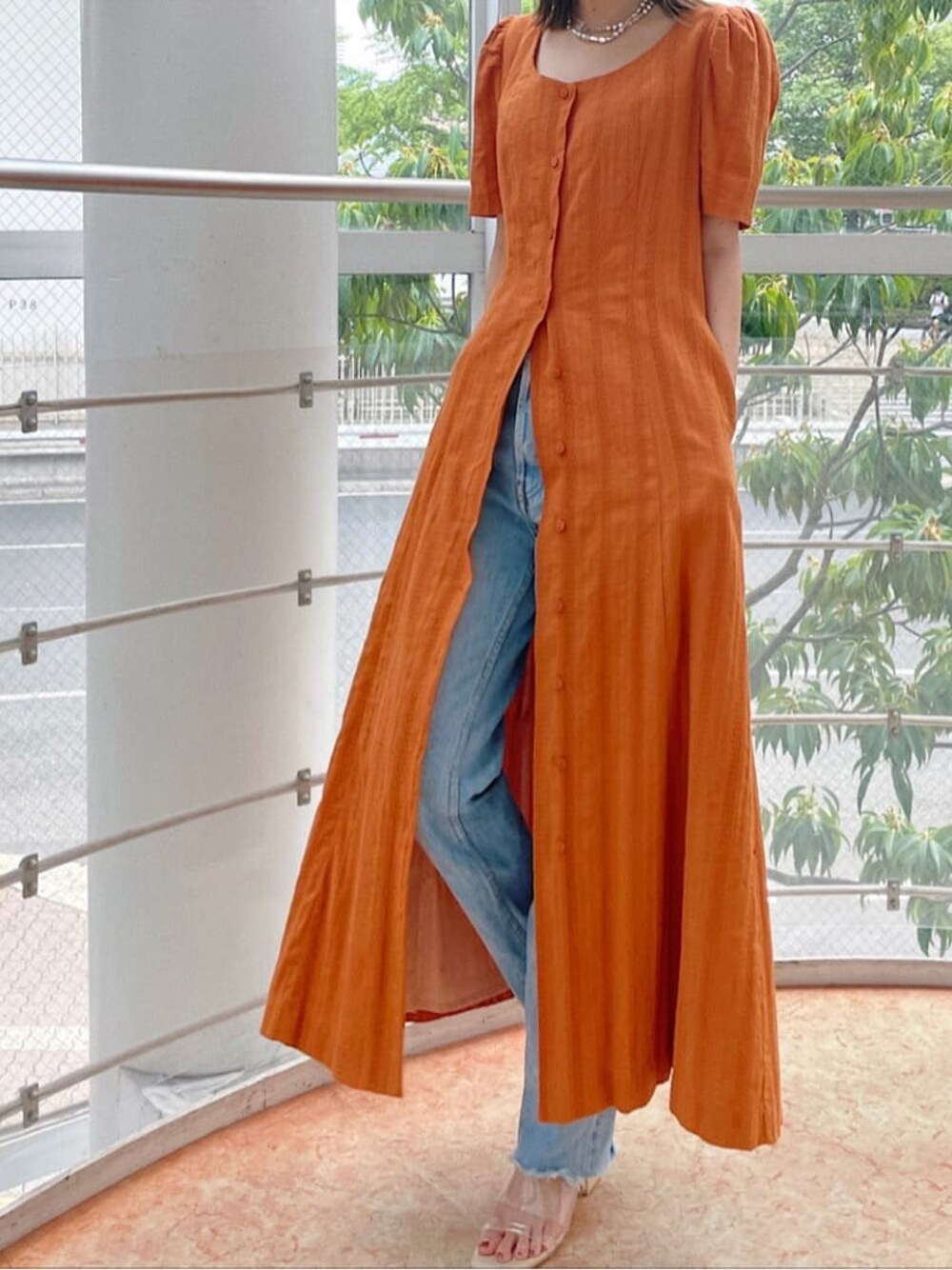 オレンジ系のワンピース、シルバー系のネックレスを着用したレディースの夏コーディネートの1枚目の写真