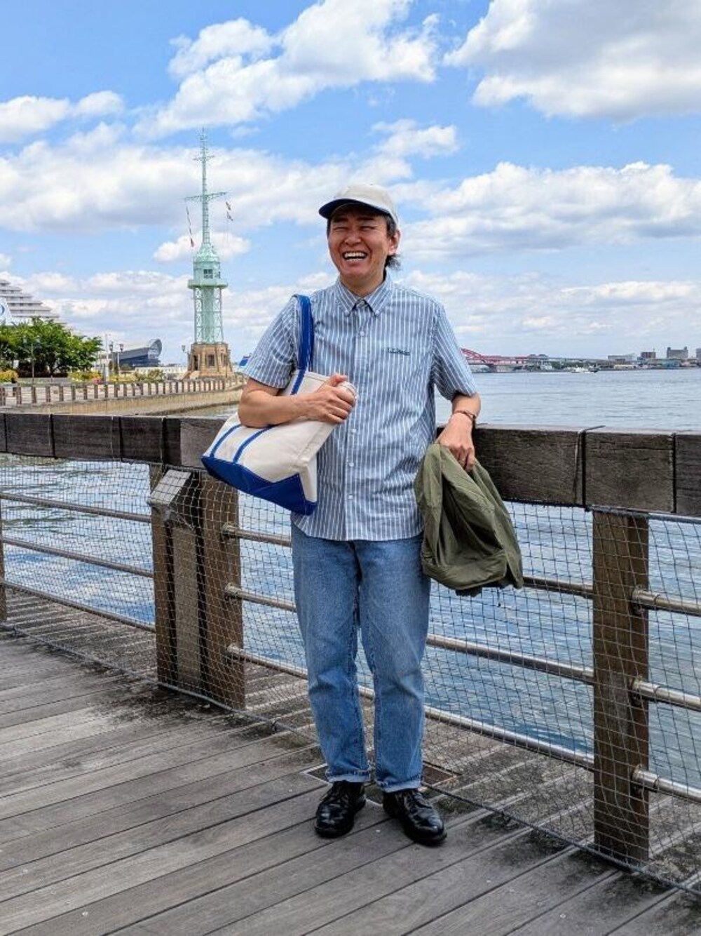 ブルー系のトートバッグ、グリーン系のナイロンジャケット、ブルー系のシャツ/ブラウスを着用したメンズの春コーディネートの1枚目の写真