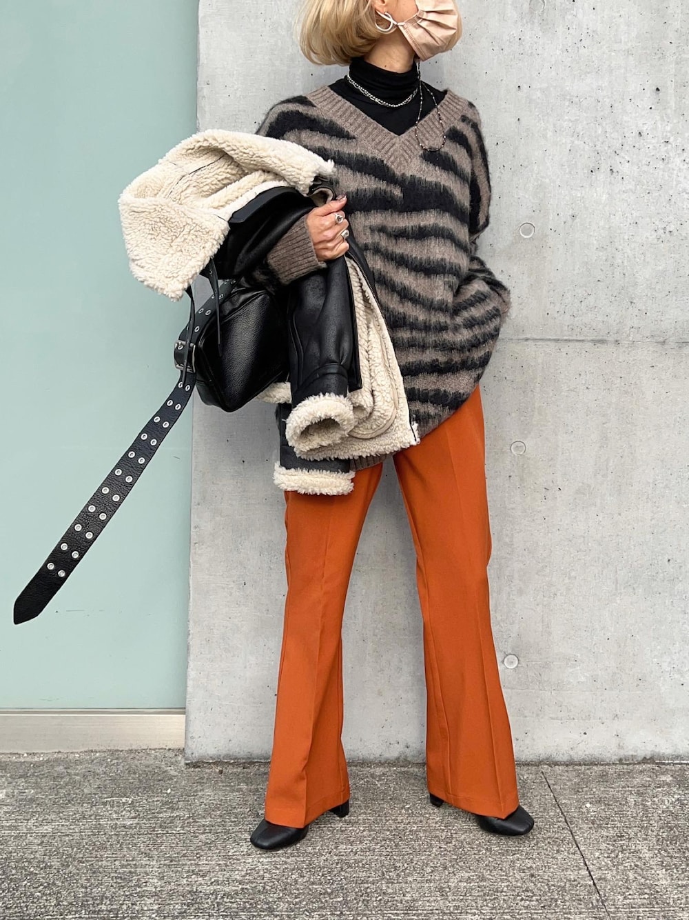オレンジ系のスラックス、ブラック系のブーツ、グレー系のニット/セーターを着用したレディースの冬コーディネートの1枚目の写真