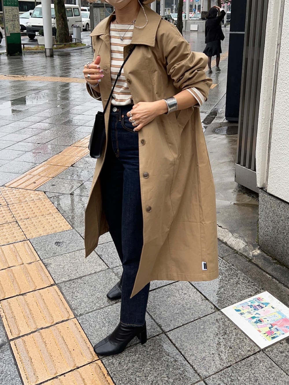 ベージュ系のトレンチコート、ブラック系のブーツ、ブルー系のデニムパンツを着用したレディースの春コーディネートの1枚目の写真