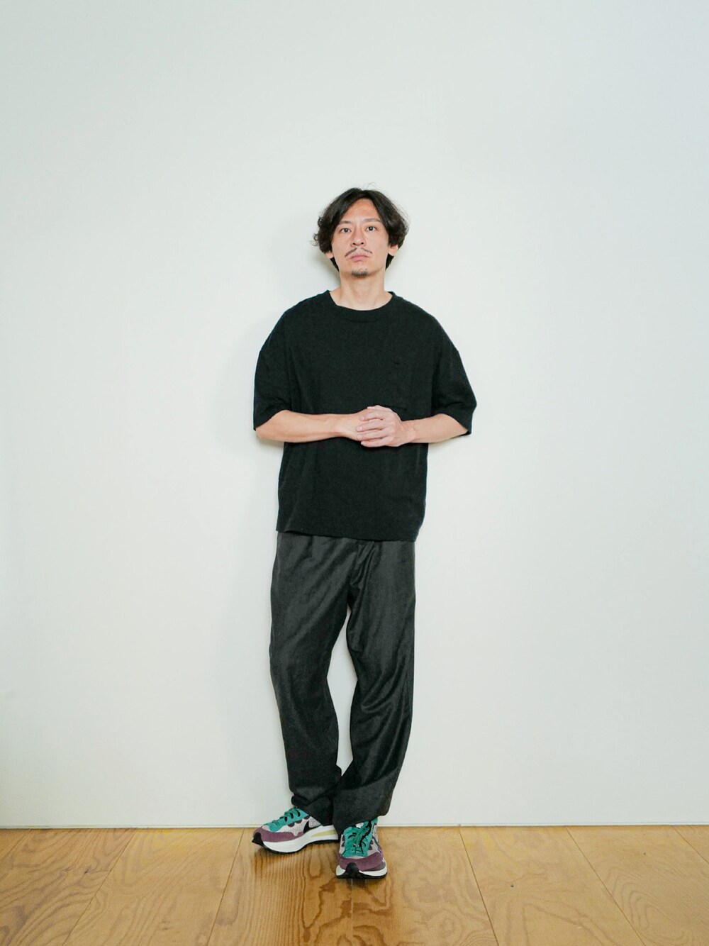ブラック系のTシャツ/カットソー、グレー系のスラックス、パープル系のスニーカーを着用したメンズの秋コーディネートの1枚目の写真