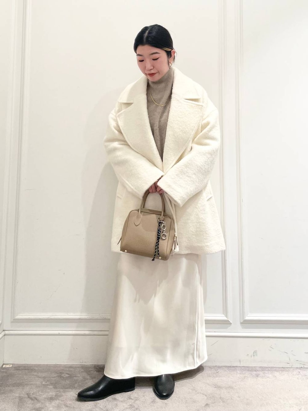 ホワイト系のピーコート、ホワイト系のスカート、ブラウン系のニット/セーターを着用したレディースの冬コーディネートの1枚目の写真