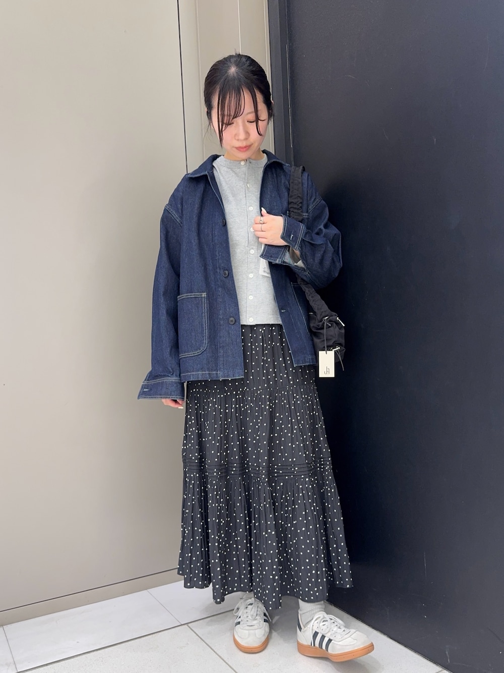 ブルー系のカバーオール、グレー系のカーディガン/ボレロ、ブラック系のスカートを着用したレディースの春コーディネートの1枚目の写真